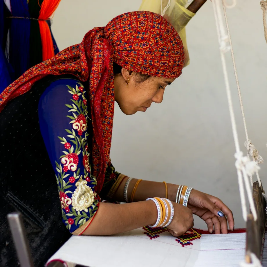 A woman weaving an embroidered fabric on a handloom